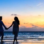 Honeymooners - Man and Woman Holding Hands Walking on Seashore during Sunrise