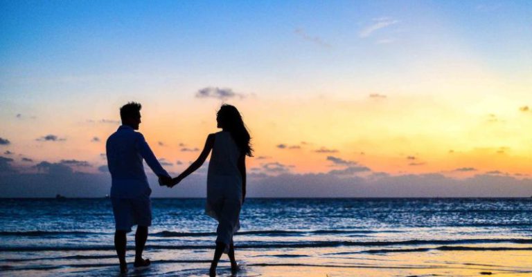 Honeymooners - Man and Woman Holding Hands Walking on Seashore during Sunrise