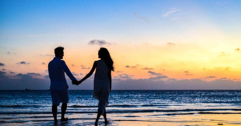 Honeymooners - Man and Woman Holding Hands Walking on Seashore during Sunrise