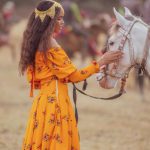 Touches - A woman in a yellow dress is petting a horse