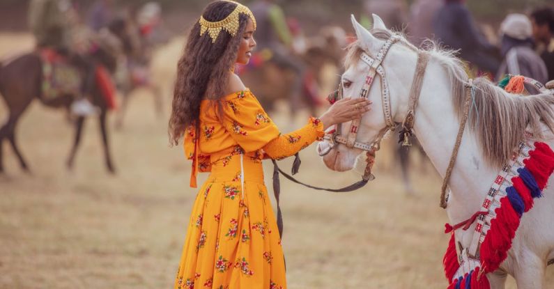 Touches - A woman in a yellow dress is petting a horse