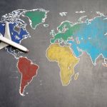 Educational Trips - Top view of crop anonymous person holding toy airplane on colorful world map drawn on chalkboard