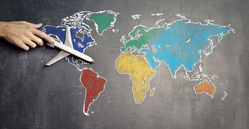 Educational Trips - Top view of crop anonymous person holding toy airplane on colorful world map drawn on chalkboard