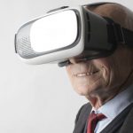 Immerse - Smiling elderly gentleman wearing classy suit experiencing virtual reality while using modern headset on white background