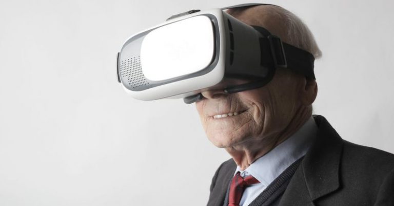 Immerse - Smiling elderly gentleman wearing classy suit experiencing virtual reality while using modern headset on white background