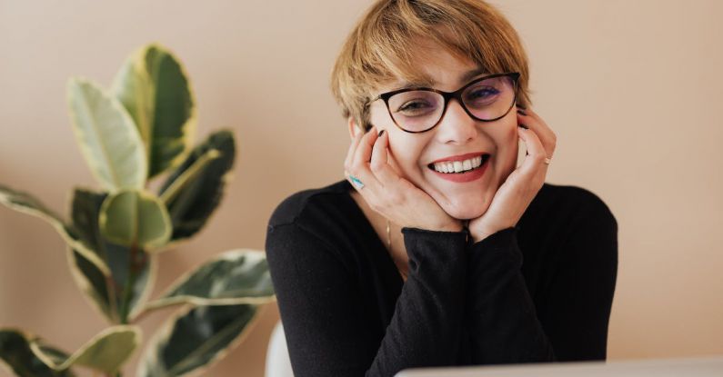 Corporate Retreats - Cheerful woman smiling while sitting at table with laptop