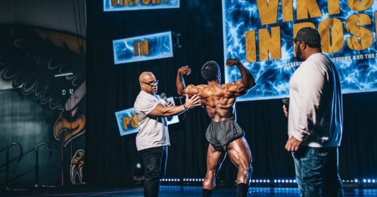 Hosts - Back view of a Shirtless Man Flexing His Muscles while on Stage